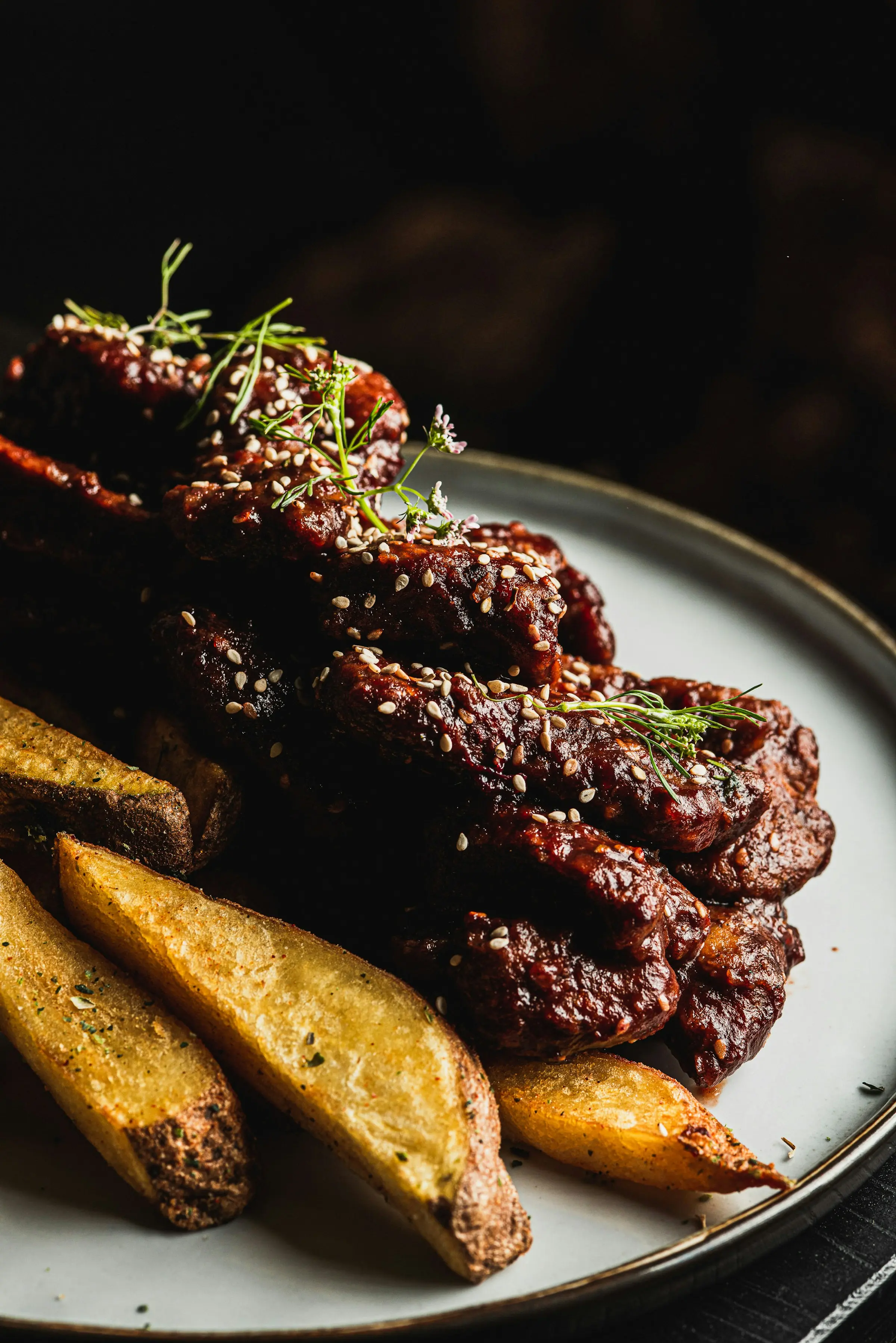 Sticky barbecue ribs with potato wedges on a dark plate