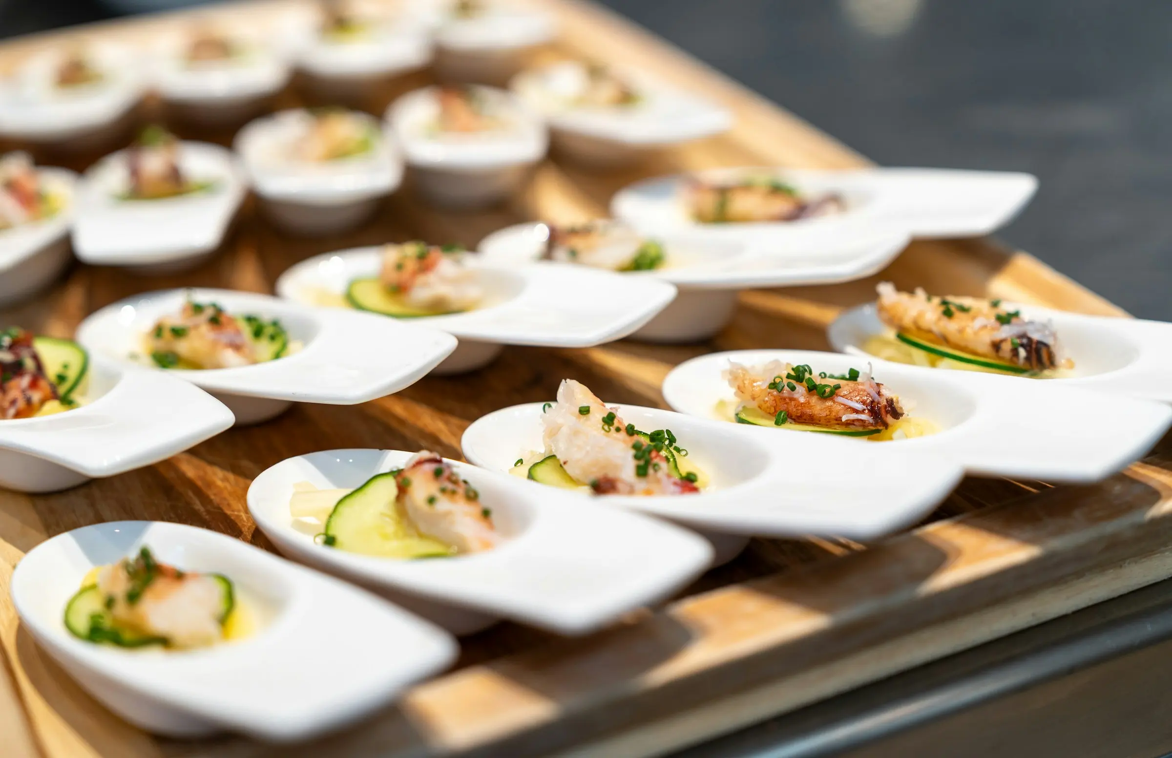 Spoon canapés with lobster and cucumber on a wooden tray