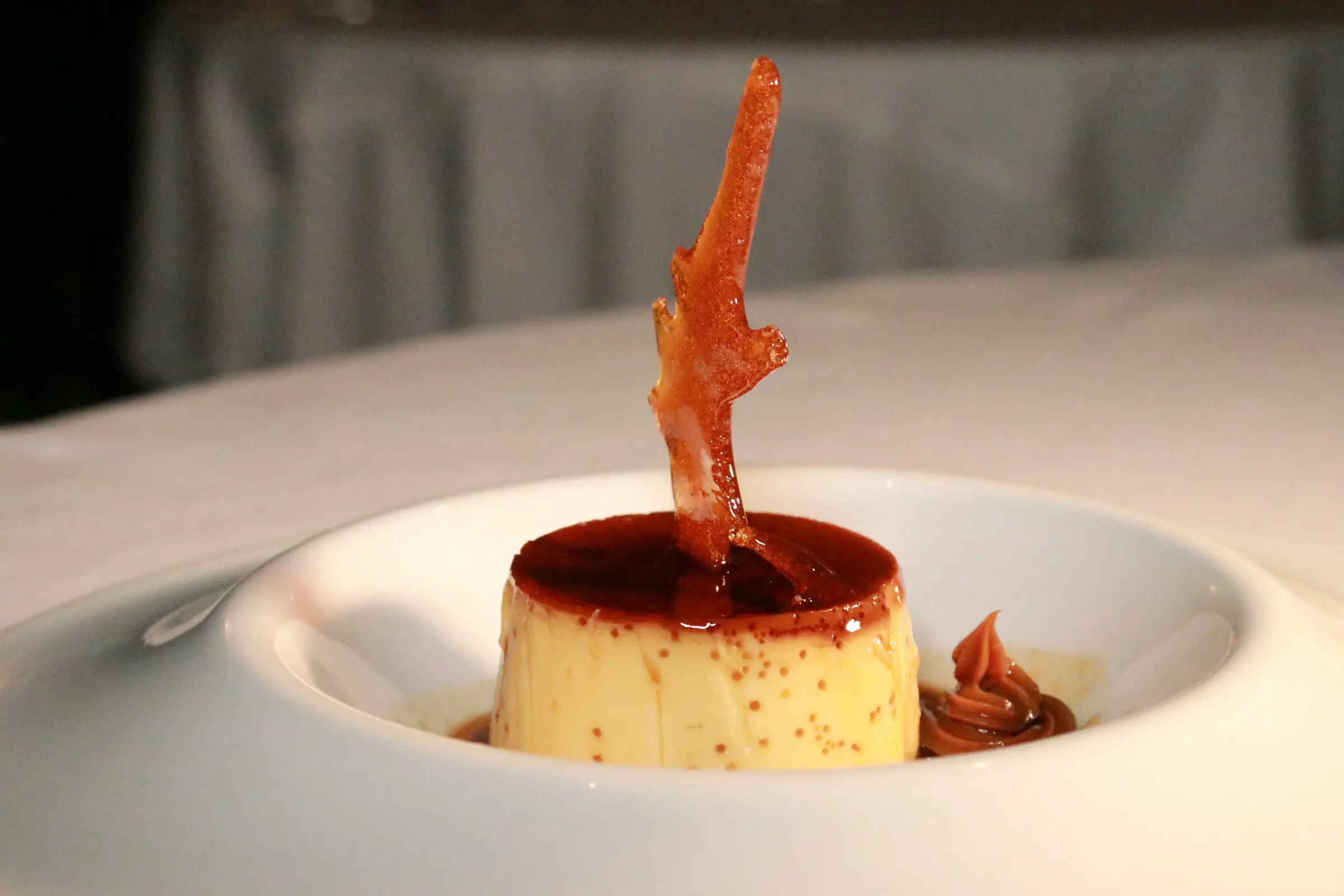 Crème caramel with a spun-sugar shard in a white bowl