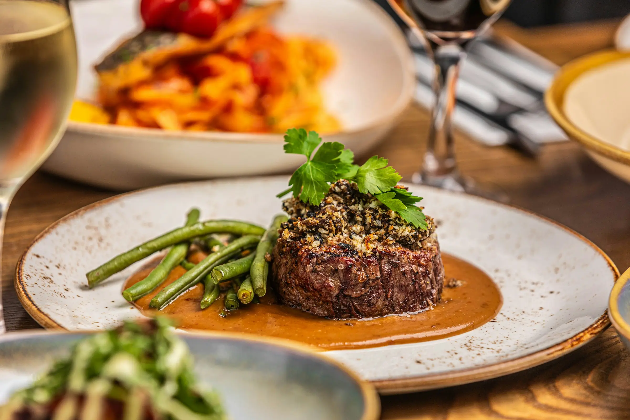 Crusted beef fillet with green beans and sauce, glass of red wine behind