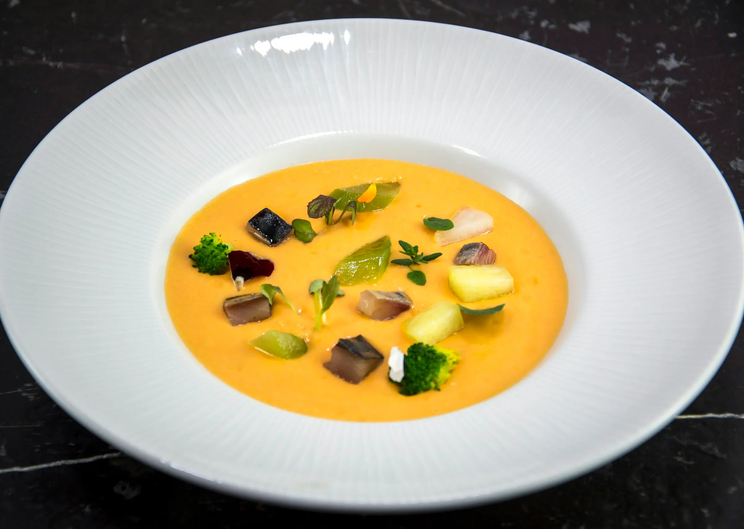 Golden velouté with vegetable garnish in a wide bowl